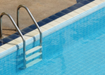 Se muestra una escalera de 3 peldaños anclada al suelo en una piscina enterrada con agua limpia