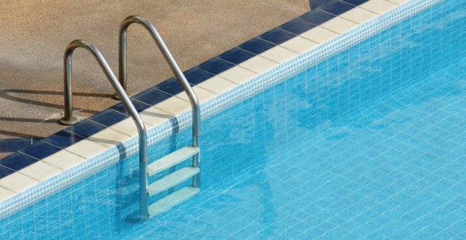 Se muestra una escalera de 3 peldaños anclada al suelo en una piscina enterrada con agua limpia